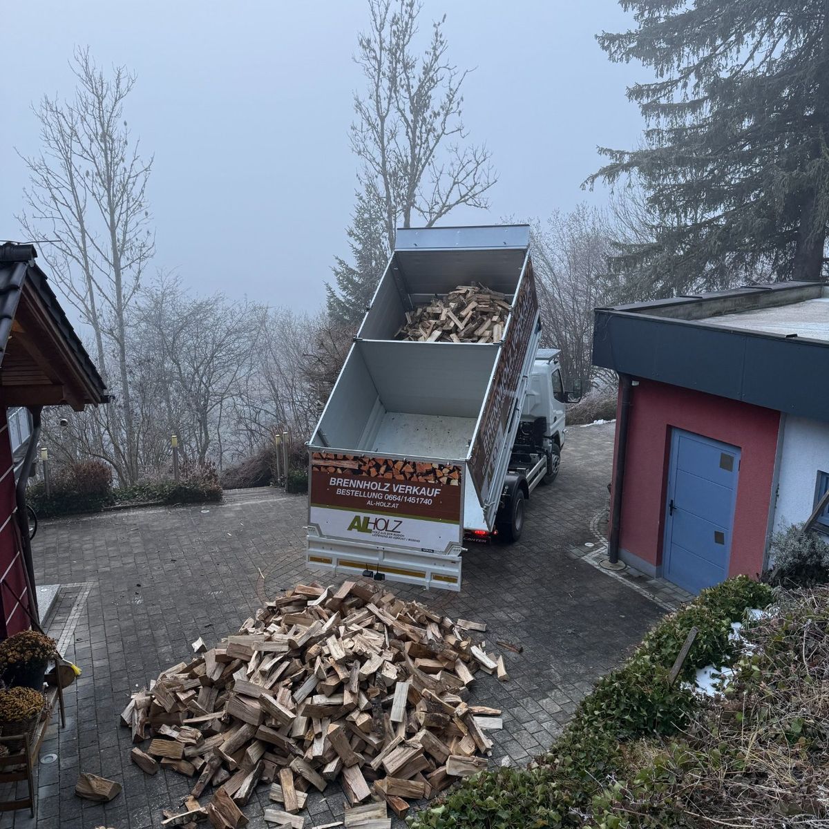 Der AL-Holz-Kipper lädt lose geschüttetes Brennholz auf einem gepflasterten Hof ab